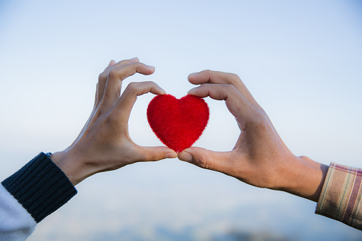 Red heart in woman and man hands, hands holding a soft heart shape, Couple love, Valentine's Day.